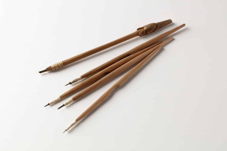 Five hand-carved wooden sticks the size of pencils with different sizes of metal tips on a white background. 