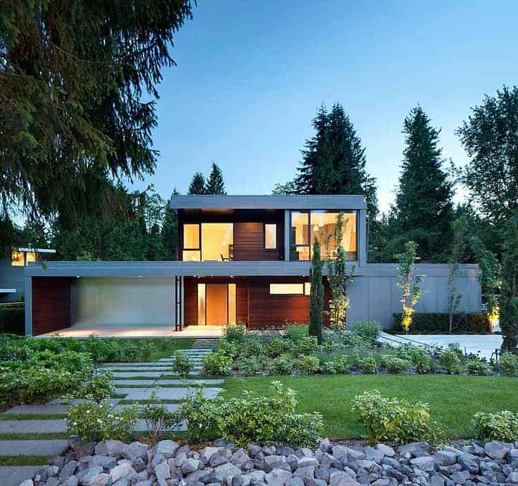 Modern luxury house with sleek design, large glass windows, and contemporary architecture surrounded by lush greenery and landscaped garden.