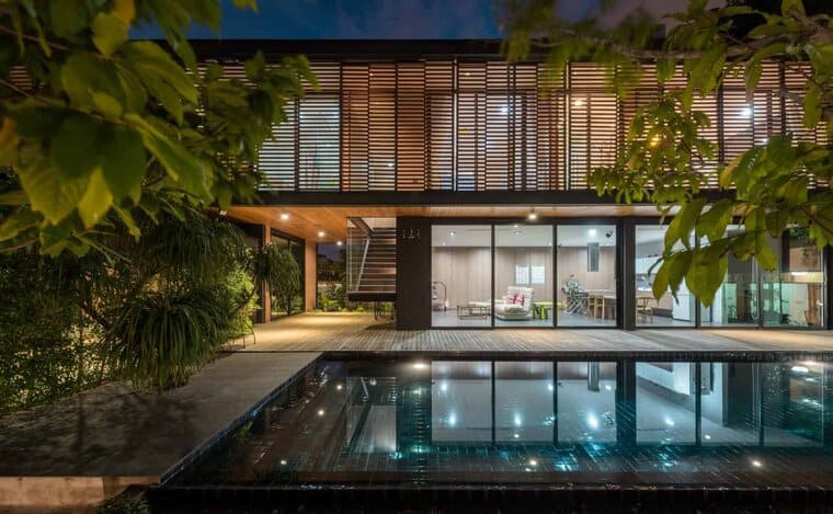 Modern house with glass walls, illuminated interior, and outdoor pool surrounded by greenery, showcasing contemporary architecture and sustainable design elements at night.