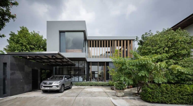Contemporary modern house with sleek architectural design featuring large glass windows, wooden accents, and a spacious driveway surrounded by lush greenery.