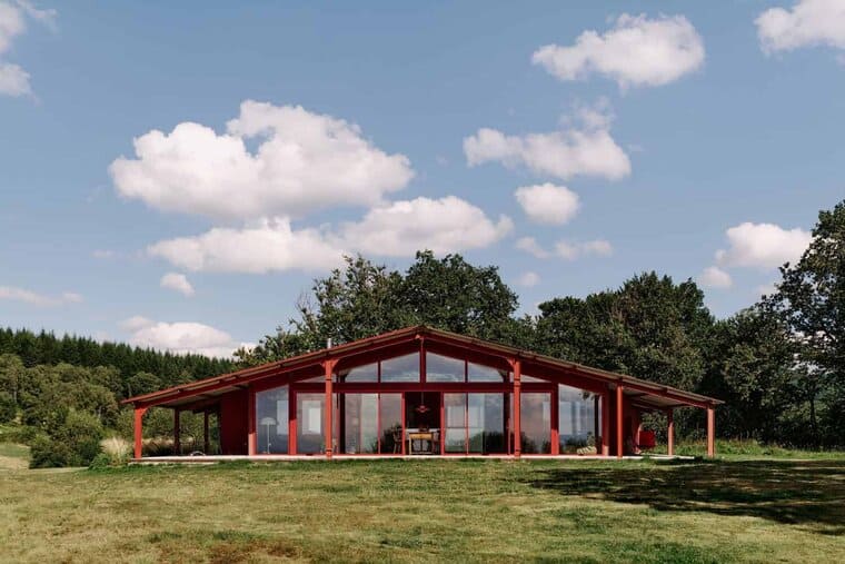 Modern red glass house with open-plan living space, surrounded by lush greenery and trees, showcasing contemporary architecture and innovative design for outdoor living.