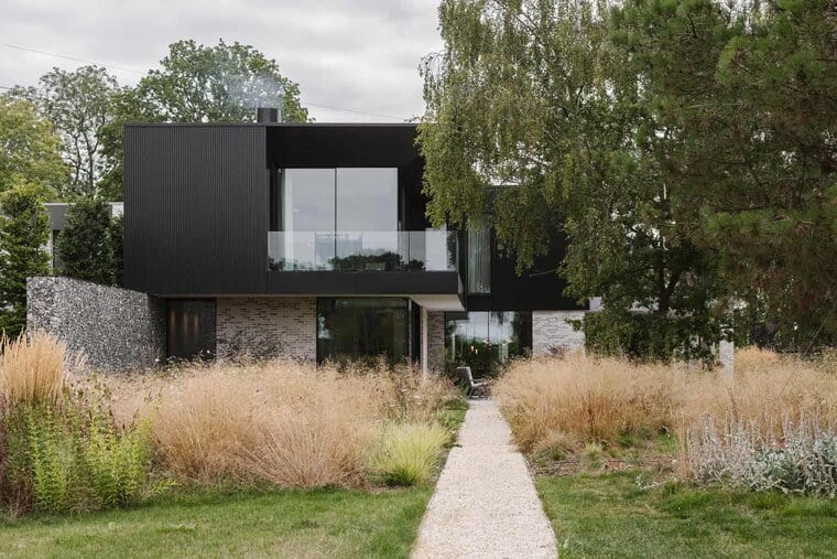 Modern black metal and brick residential house with large glass windows, surrounded by landscaped garden and pathway, showcasing contemporary architecture and innovative design.