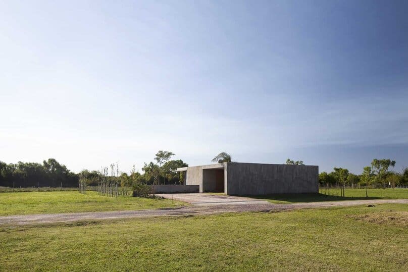 Modern minimalist concrete house in a lush green landscape under a clear blue sky.
