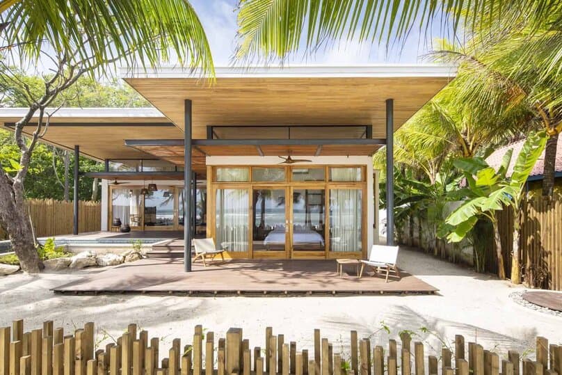 Modern tropical beach house with open-concept design, wood accents, large glass doors, and lush landscaping. Perfect for seaside living and outdoor relaxation.