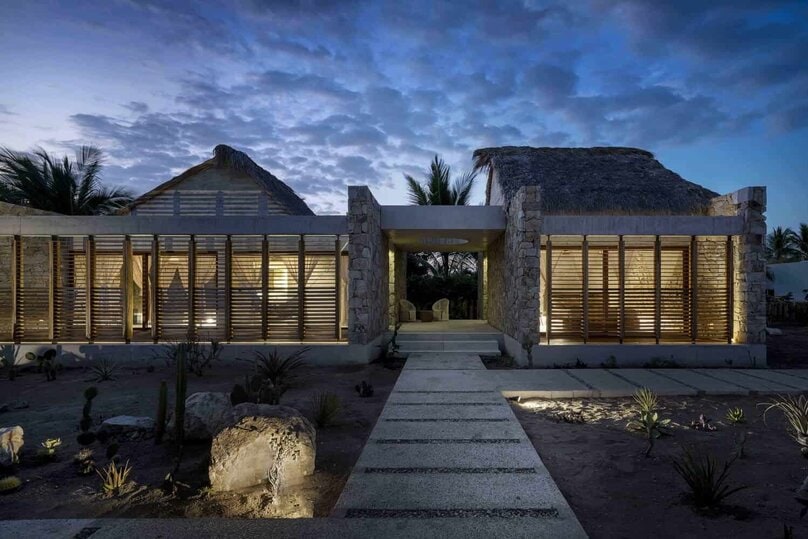 Modern desert-inspired house with stone and wooden architectural elements at dusk. Stunning home design blending natural materials with contemporary style in a warm, inviting outdoor setting.