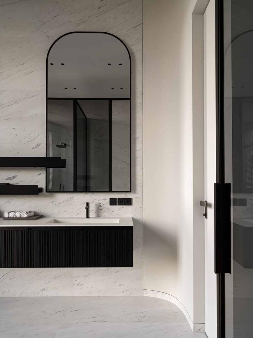 Bathroom with arched mirror and floating vanity set against marble walls.