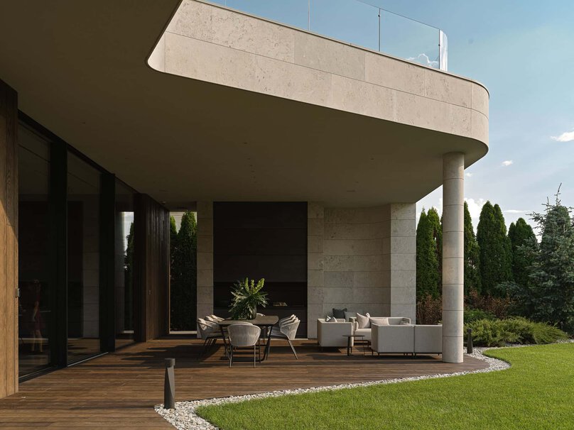Spacious covered terrace with outdoor lounge and dining set surrounded by greenery.