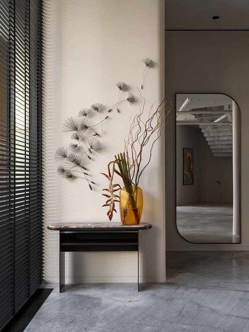 Yellow glass vase with sculptural dried florals on a console in a minimalist space.