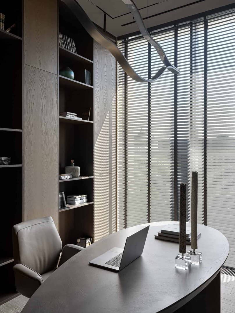 Curved executive desk in front of floor-to-ceiling bookshelves and large windows.