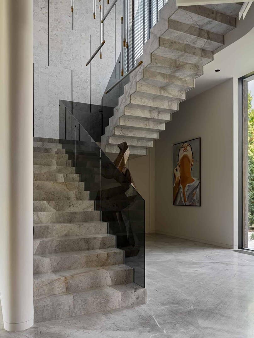 Floating stone staircase with glass railing in modern entryway.