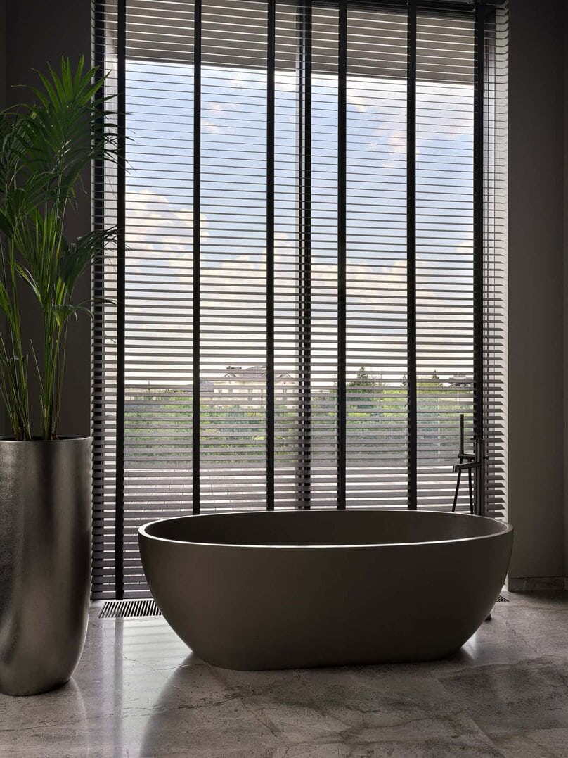 Elegant freestanding bathtub positioned beneath a large window with blinds.