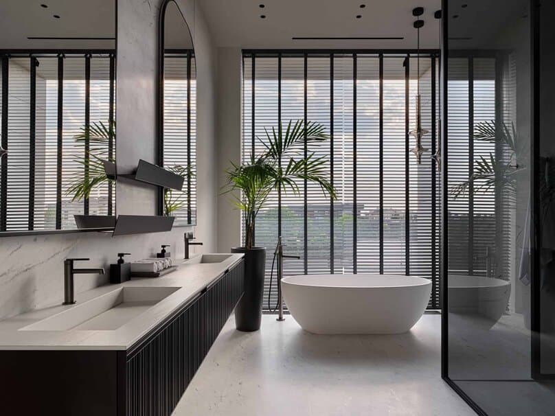 Freestanding bathtub positioned before full-height windows with vertical blinds.
