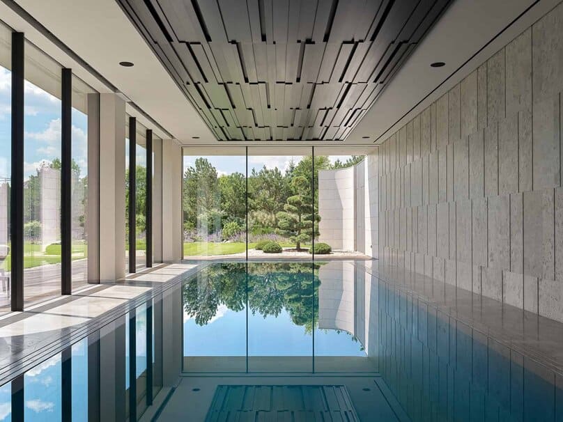 Sleek indoor swimming pool with floor-to-ceiling glass offering a lush garden view.