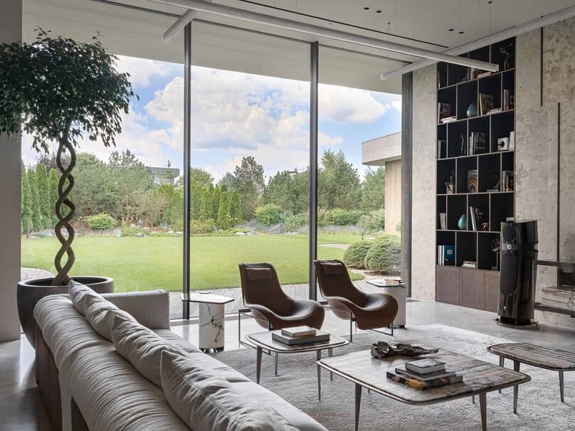 Modern leather chairs in living room facing floor-to-ceiling glass with garden view.