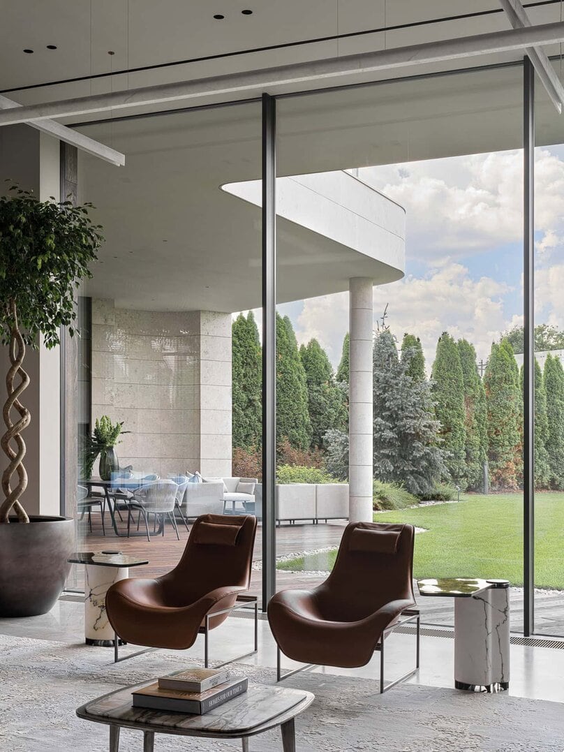 Elegant leather lounge chairs facing floor-to-ceiling windows overlooking garden.