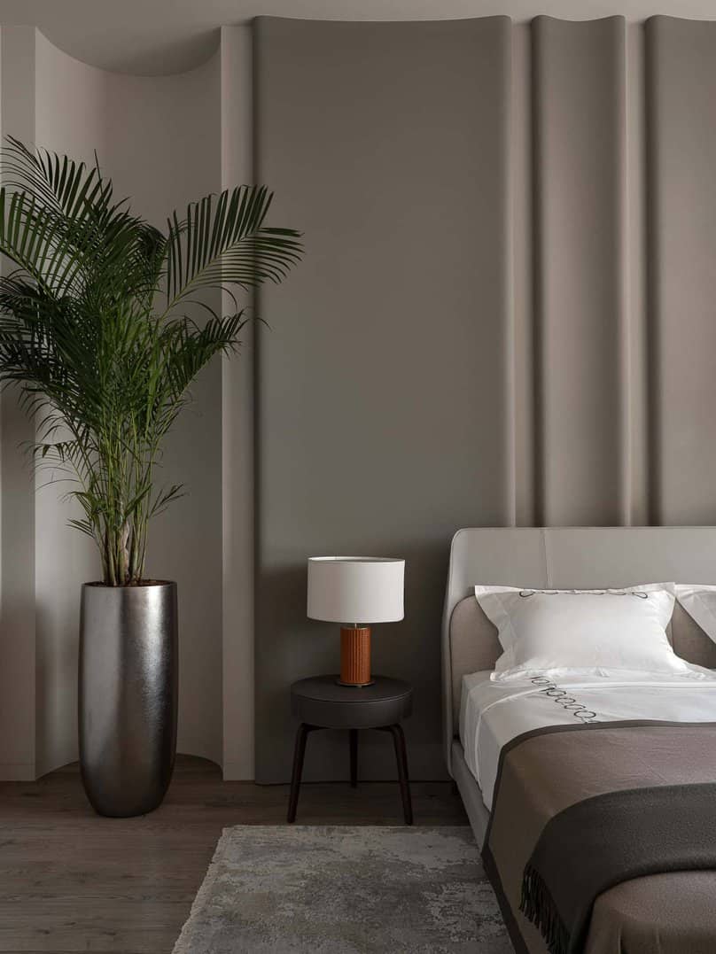 Detail view of tall palm in planter beside modern nightstand with table lamp.