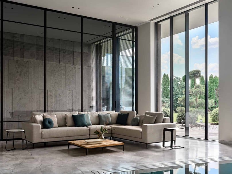 Neutral corner sofa near indoor pool with expansive garden view through glass.