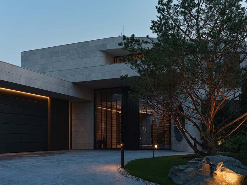 Contemporary stone villa entrance with dramatic night lighting and trees.