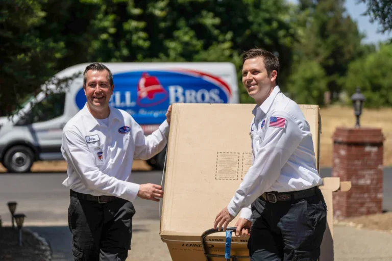 Two uniformed, background-checked technicians carry a box in Sacramento by a Bell Brothers van—trusted for upfront pricing and No Surprise Guarantee.