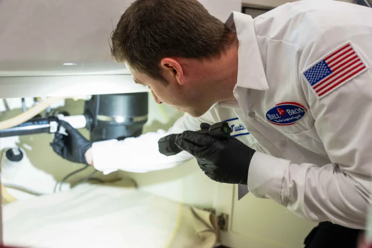 A trusted, background-checked Bell Brothers plumber inspects pipes under a sink—upfront pricing, no surprises, serving NorCal homes.