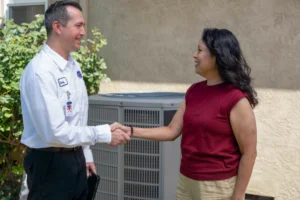 A Bell Brothers technician, background-checked and in uniform, greets a woman by her AC unit, reflecting trusted service and upfront pricing.