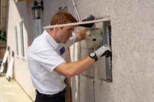 A Bell Brothers technician, background-checked and in uniform, inspects an outdoor panel—upfront pricing, No Surprise Guarantee!.