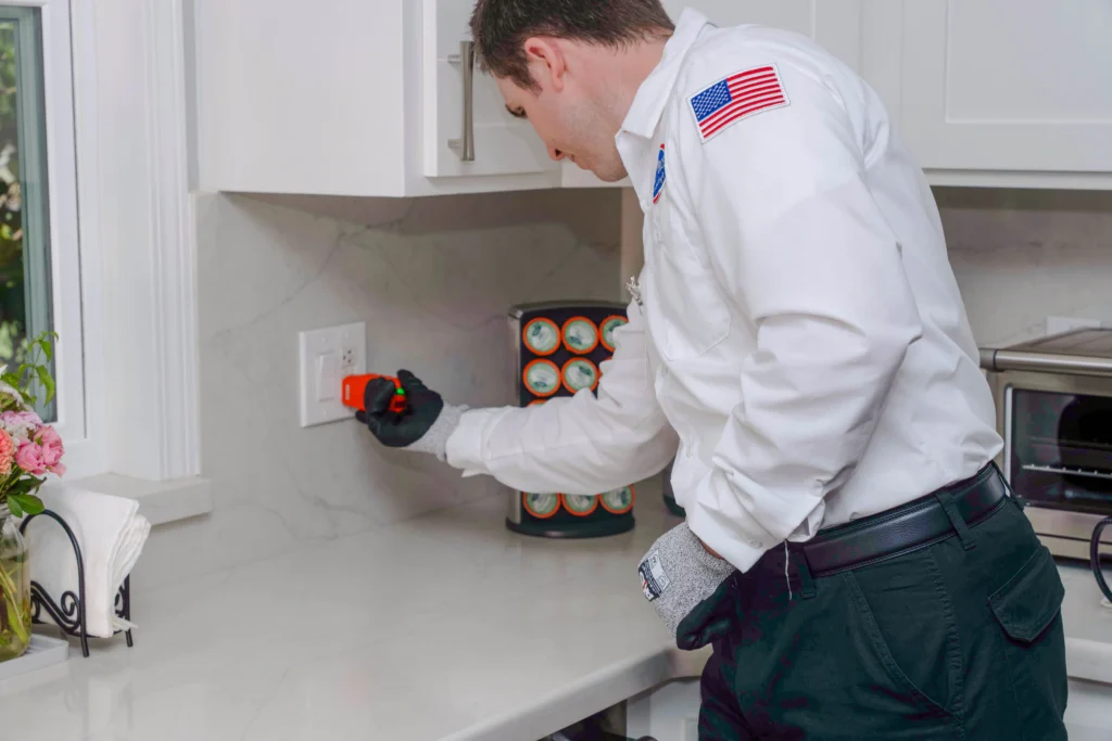 A trusted, background-checked Bell Brothers technician tests a kitchen outlet, ensuring safe upgrades with upfront pricing and no surprises.