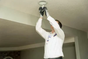 A Bell Brothers technician, uniformed and gloved, safely installs a ceiling light, assuring upfront pricing and No Surprise Guarantee.