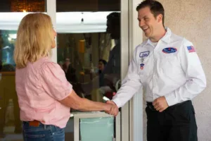 A Bell Brothers technician with a trustworthy smile greets a homeowner by her door, offering upfront pricing and the No Surprise Guarantee.