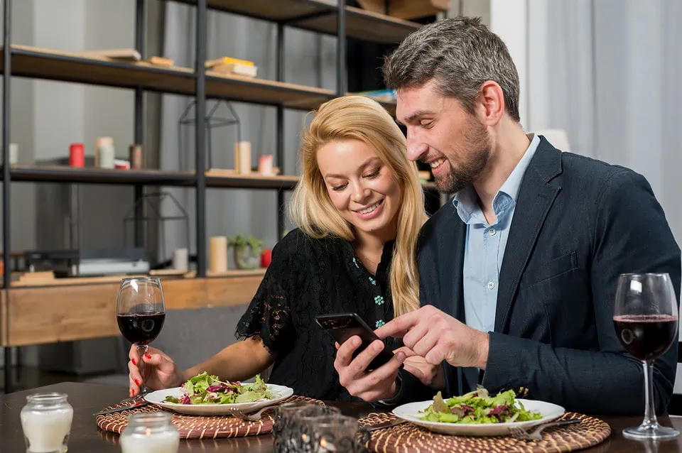 A young couple laughing while looking at a smartphone in a restaurant, representing casual dating and local hookups.
