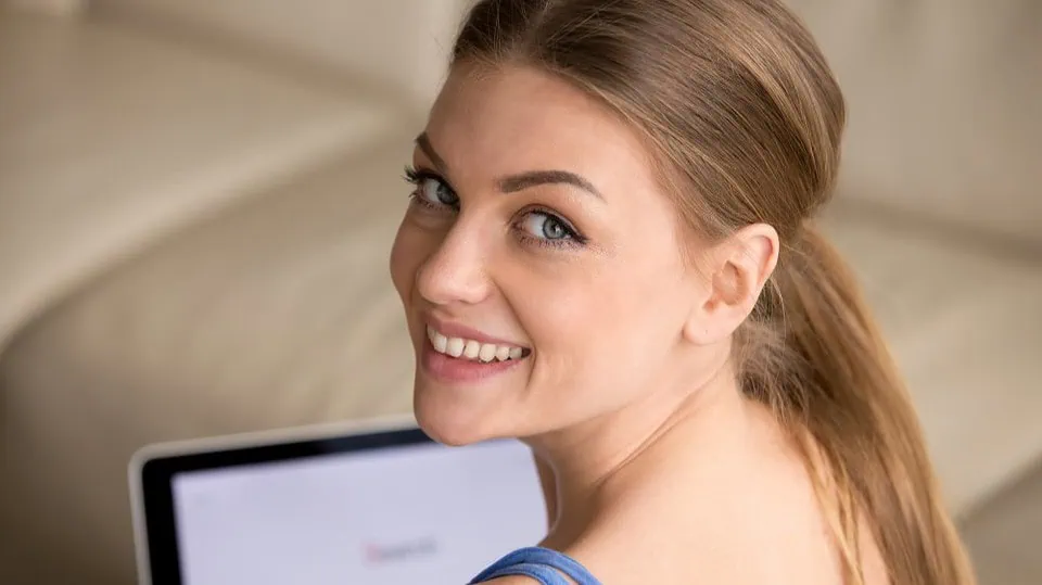 A confident woman smiling warmly during a video call on his laptop in a well-lit room.