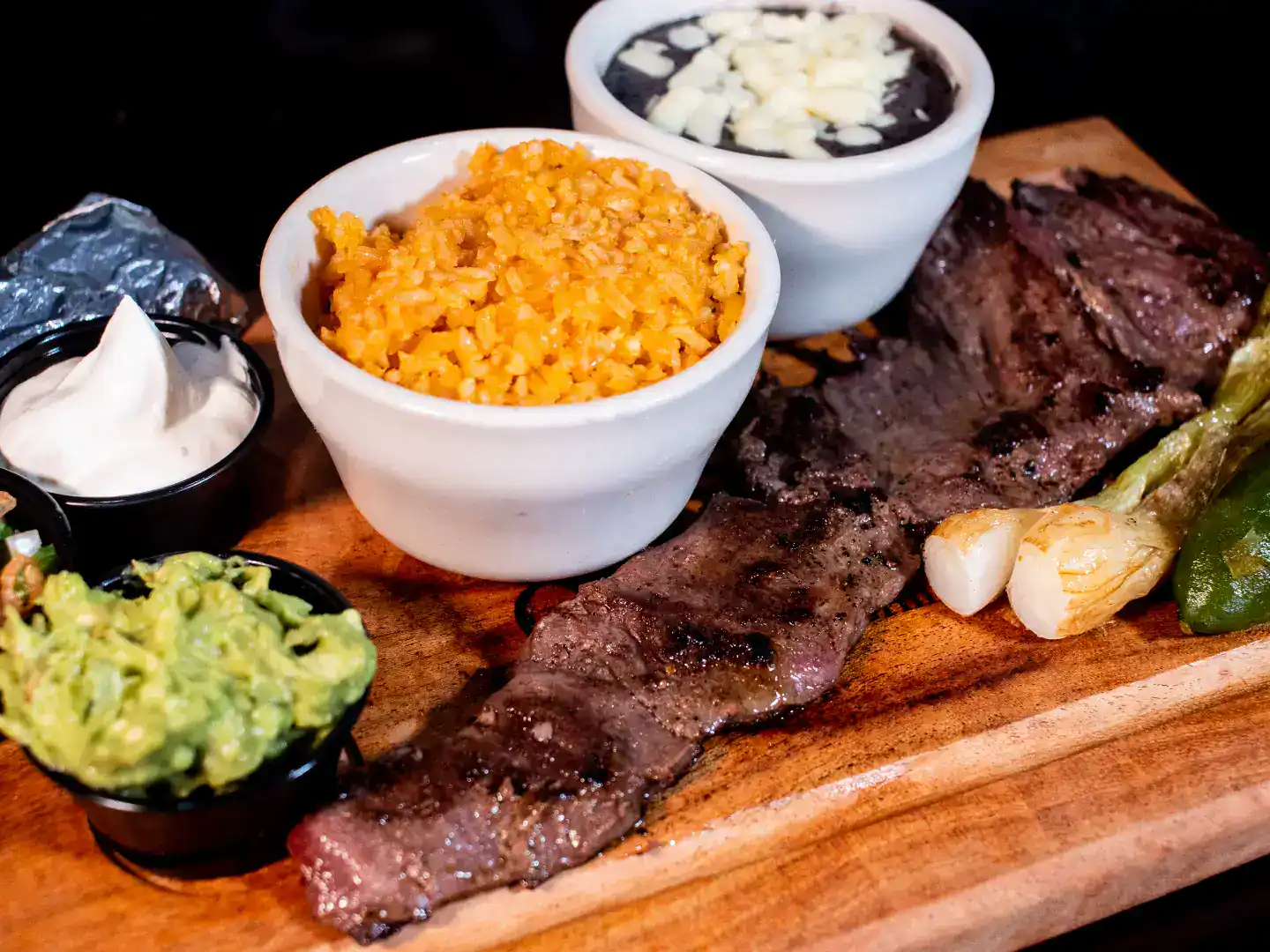 Steak with Mexican rice and sides on wooden platter.