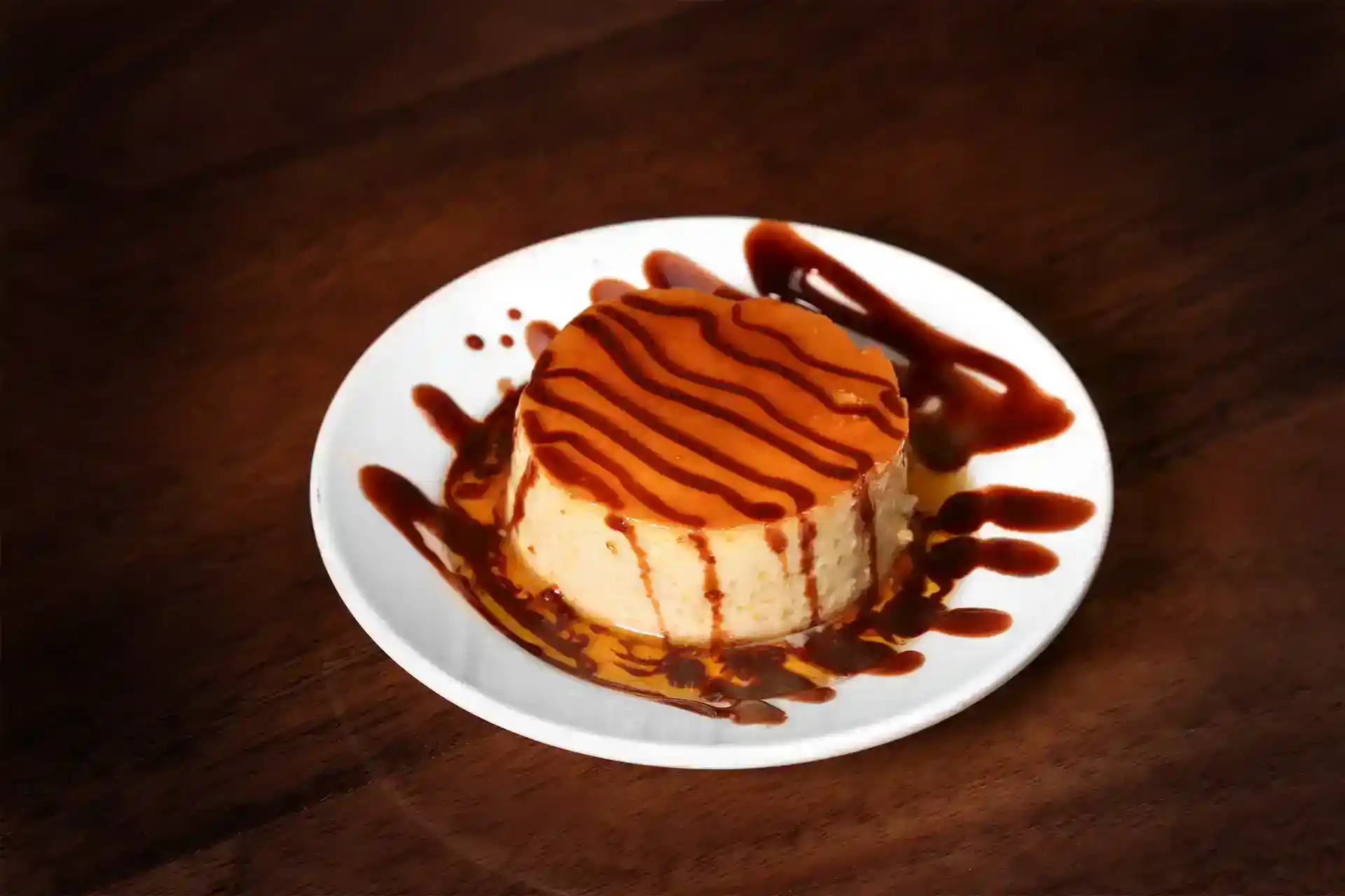 Delicious caramel flan dessert drizzled with caramel sauce on a white plate.