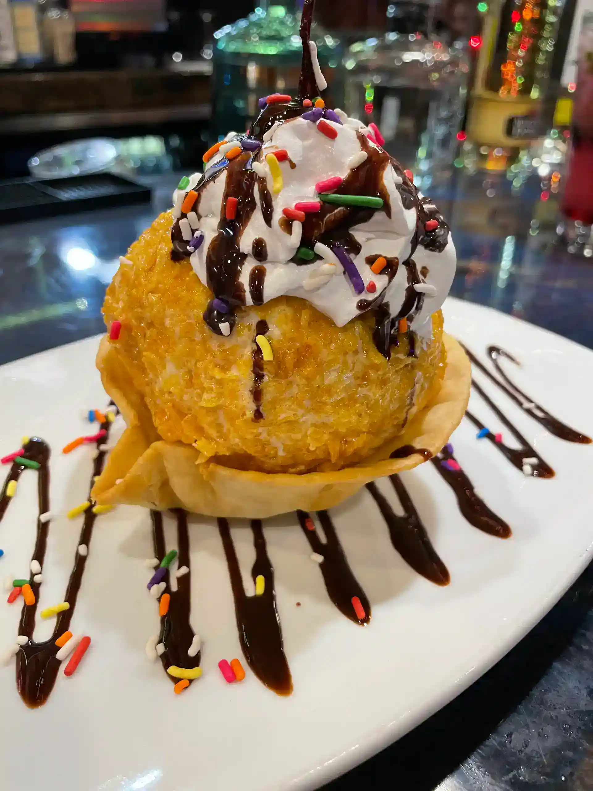 Delicious fried ice cream topped with whipped cream, chocolate syrup, and colorful sprinkles.