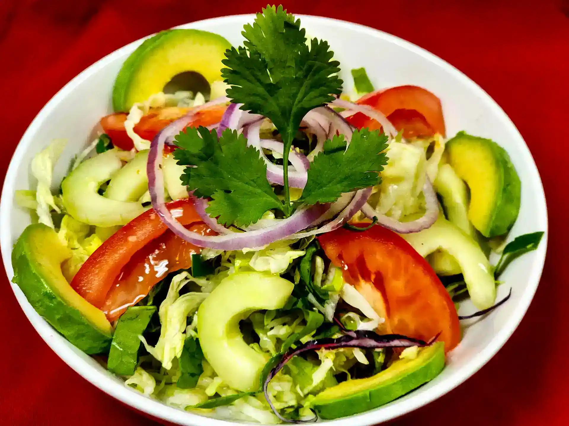 Fresh Mexican salad with avocado, tomato, cucumber, red onion, and cilantro in a white bowl.