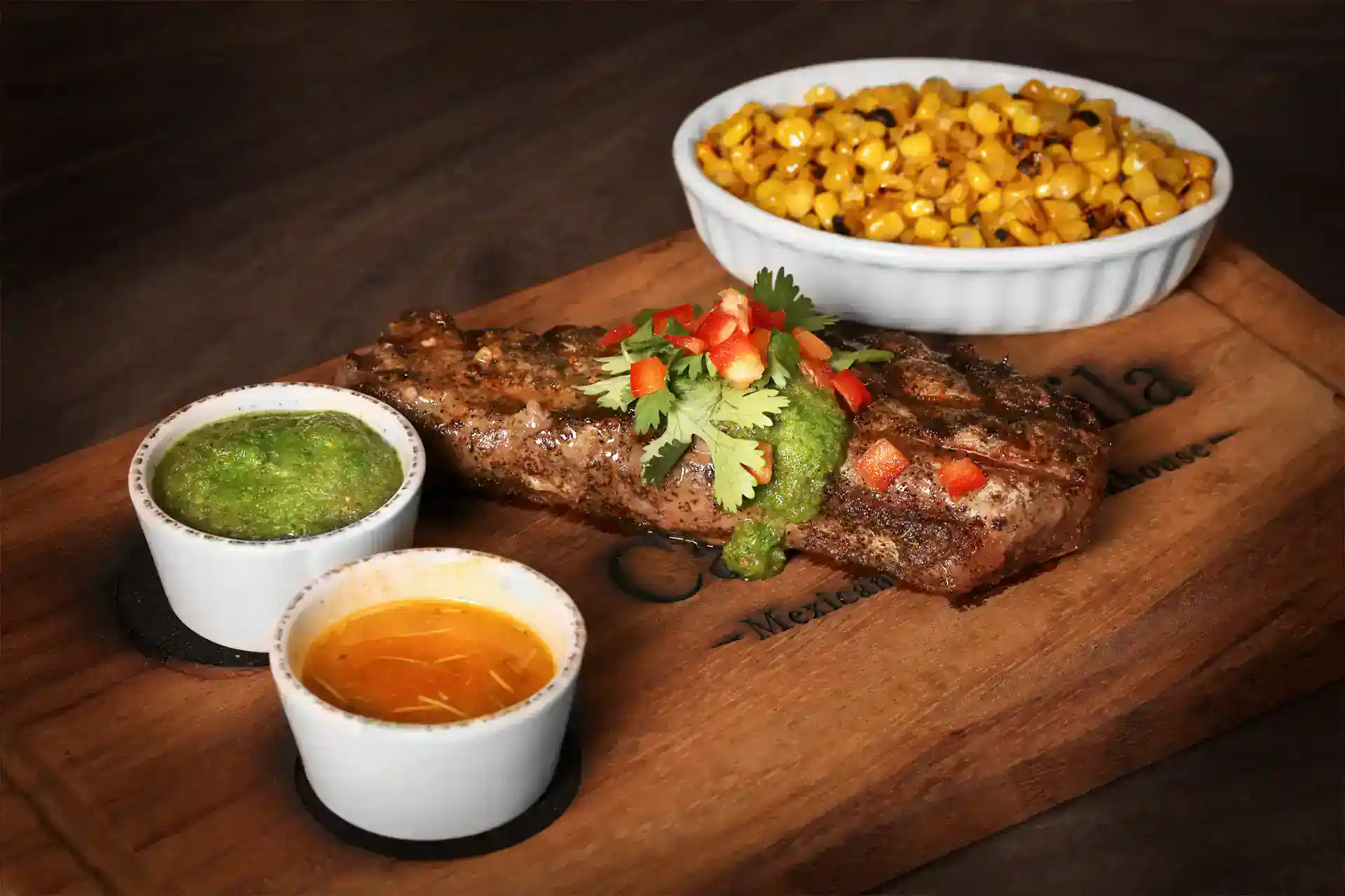 Grilled fish served with corn, green sauce, and orange sauce on a wooden board.