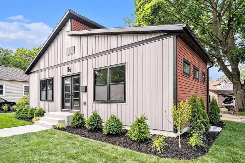 Contemporary custom home with gray and red siding, large windows, and landscaped yard.