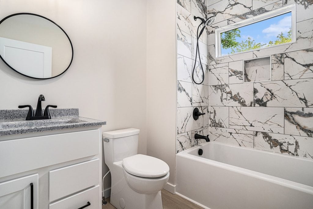 Contemporary bathroom with marble wall tiles, bathtub, and vanity with mirror.