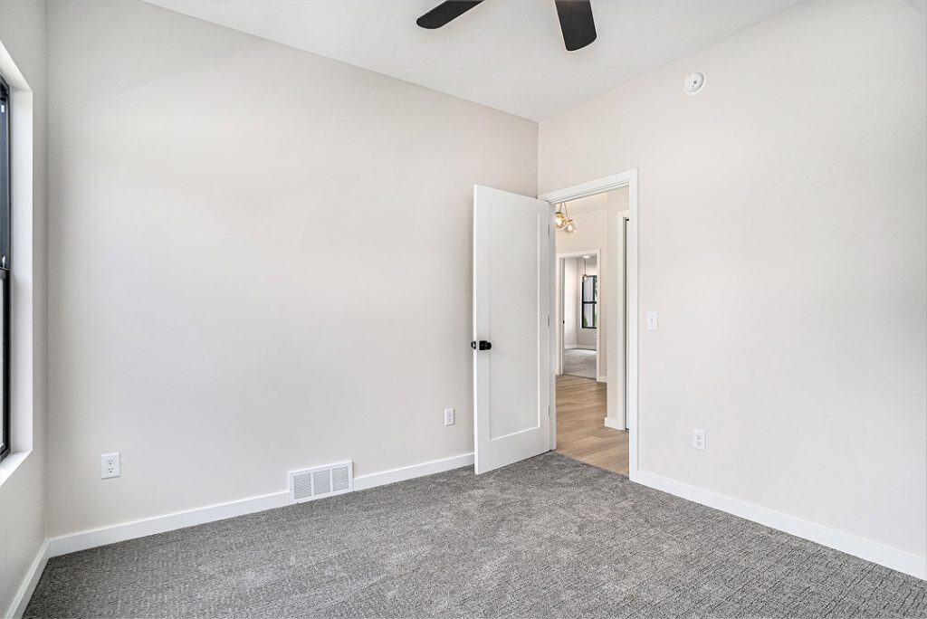Empty room with white walls, gray carpet, and open door in BuildWest Custom Homes.
