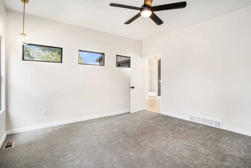 Bright modern living room with white walls, ceiling fan, and gray carpet.