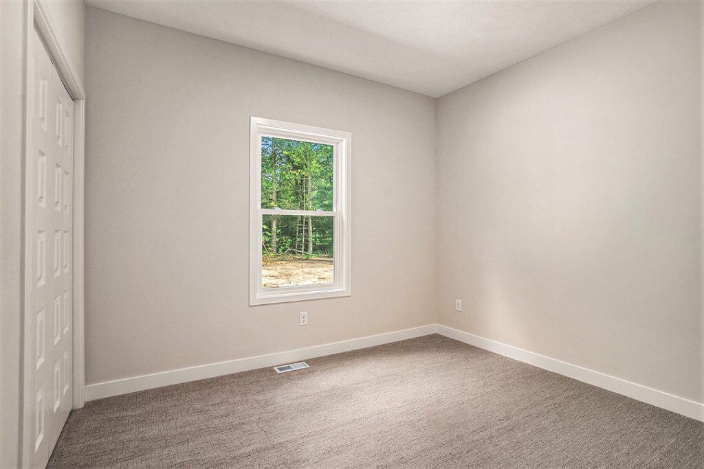 Bright empty bedroom with window and beige carpet in new home.