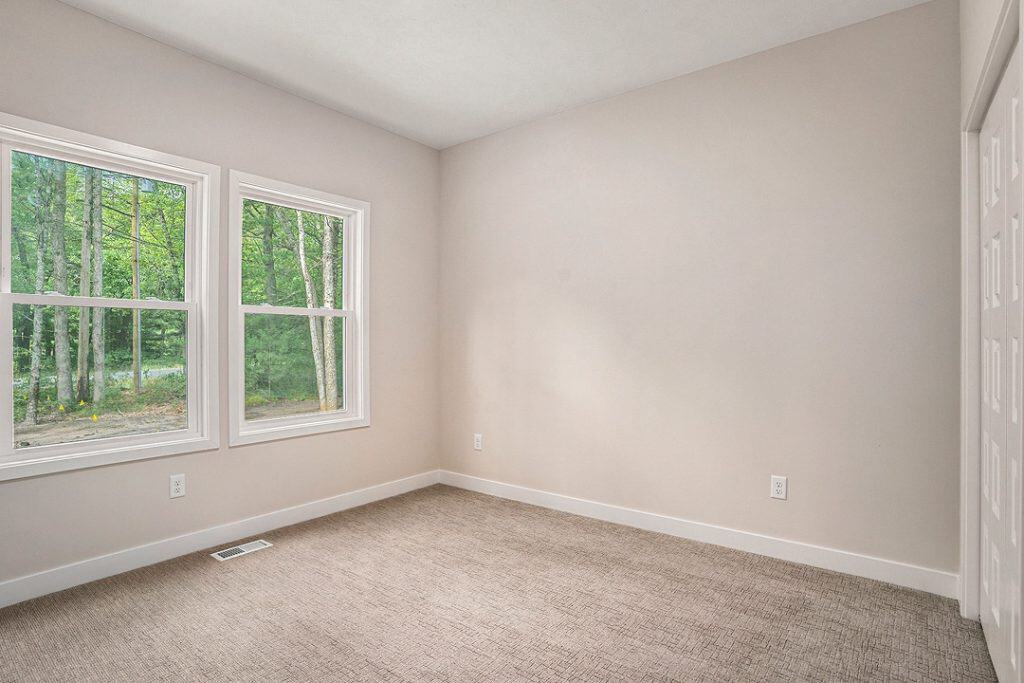 Bright empty room with large windows and beige carpet flooring.
