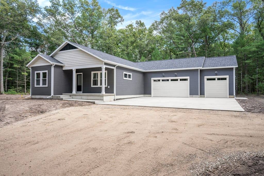 New custom-built home with gray siding and attached garage in a wooded area.