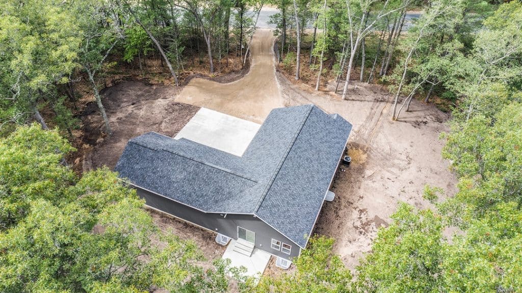 Aerial view of a modern house built by BuildWest Custom Homes in a wooded area.
