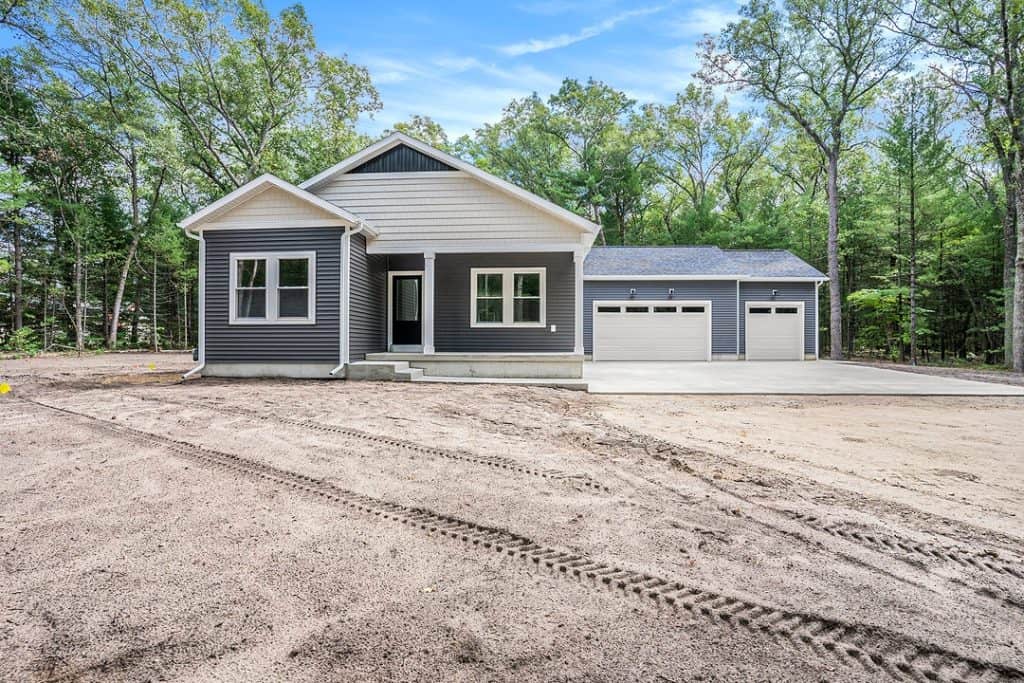 Newly built modern home with gray siding and two-car garage in a wooded area.