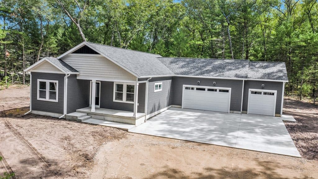 Newly built modern home with attached garage and front porch in a wooded area.