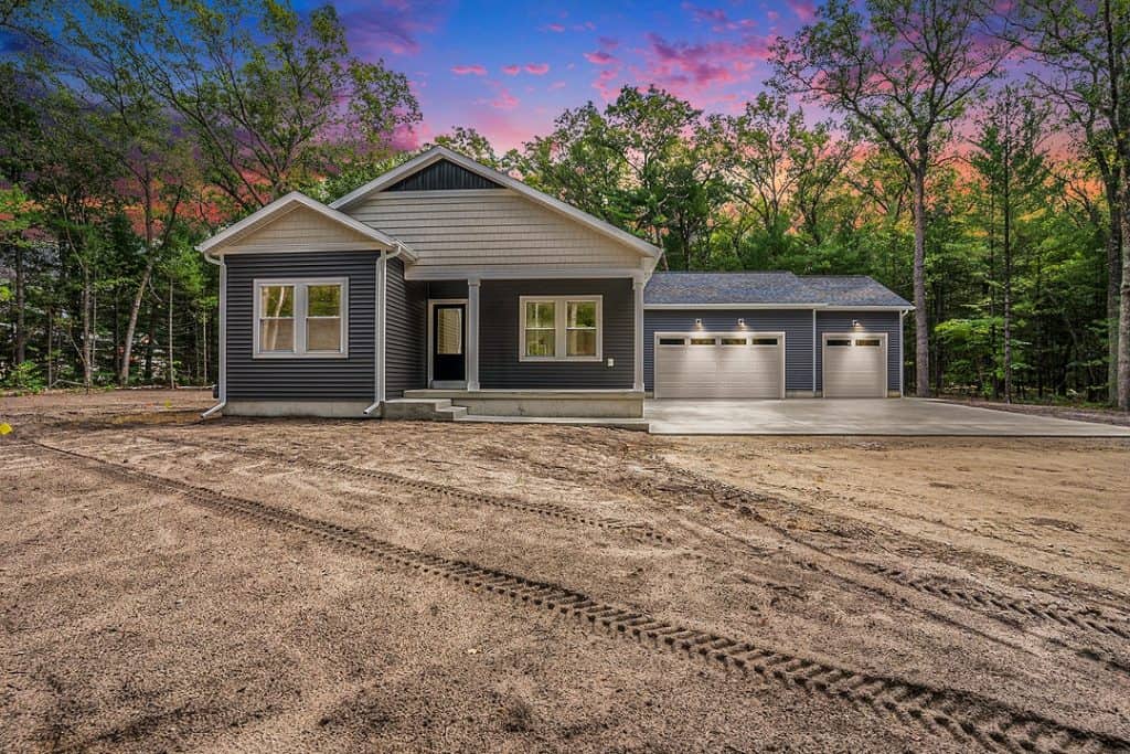 Newly built modern custom home with attached garage and scenic sunset background.