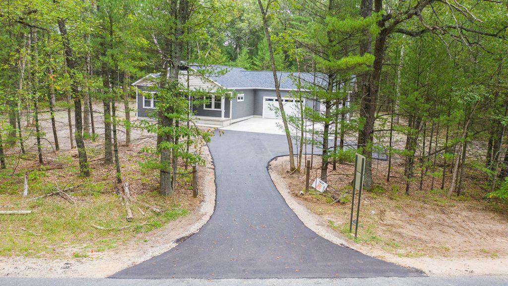 Modern custom home with paved driveway surrounded by trees.