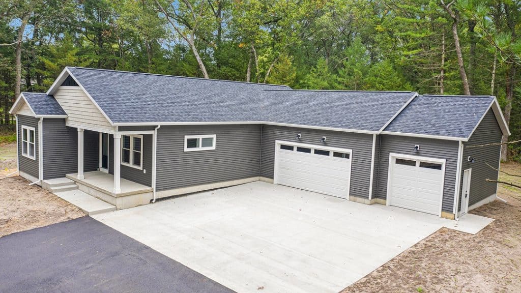 Contemporary custom home with gray siding and three-car garage in a wooded area.