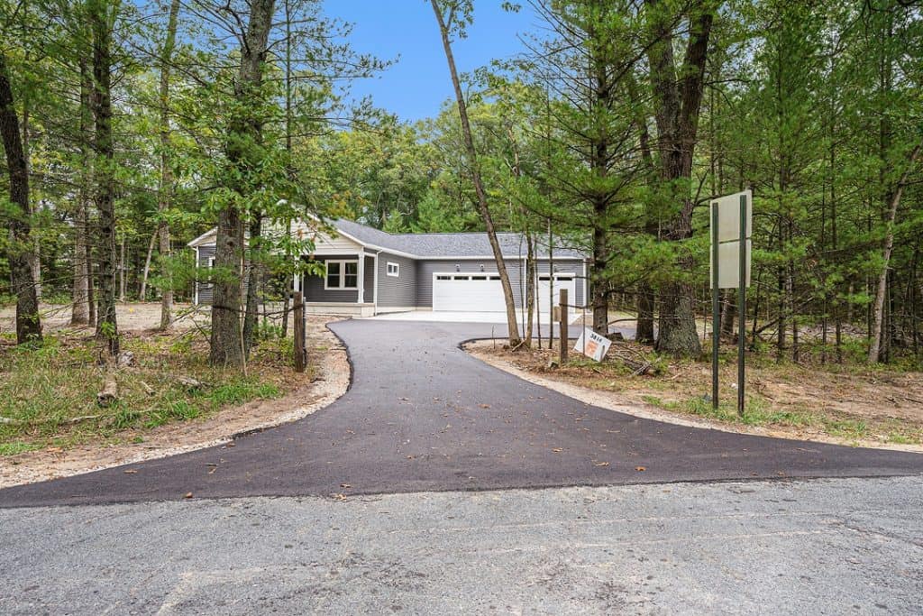 Newly built modern home with driveway in wooded area.